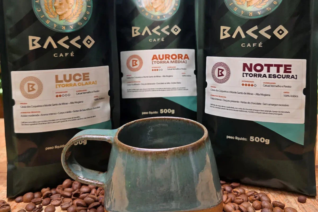 Três pacotes de café Bacco Café lado a lado com uma xícara de porcelana da marca à frente sobre grãos de café